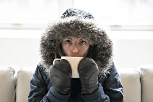 woman-wears-parka-on-couch-sips-hot-beverage